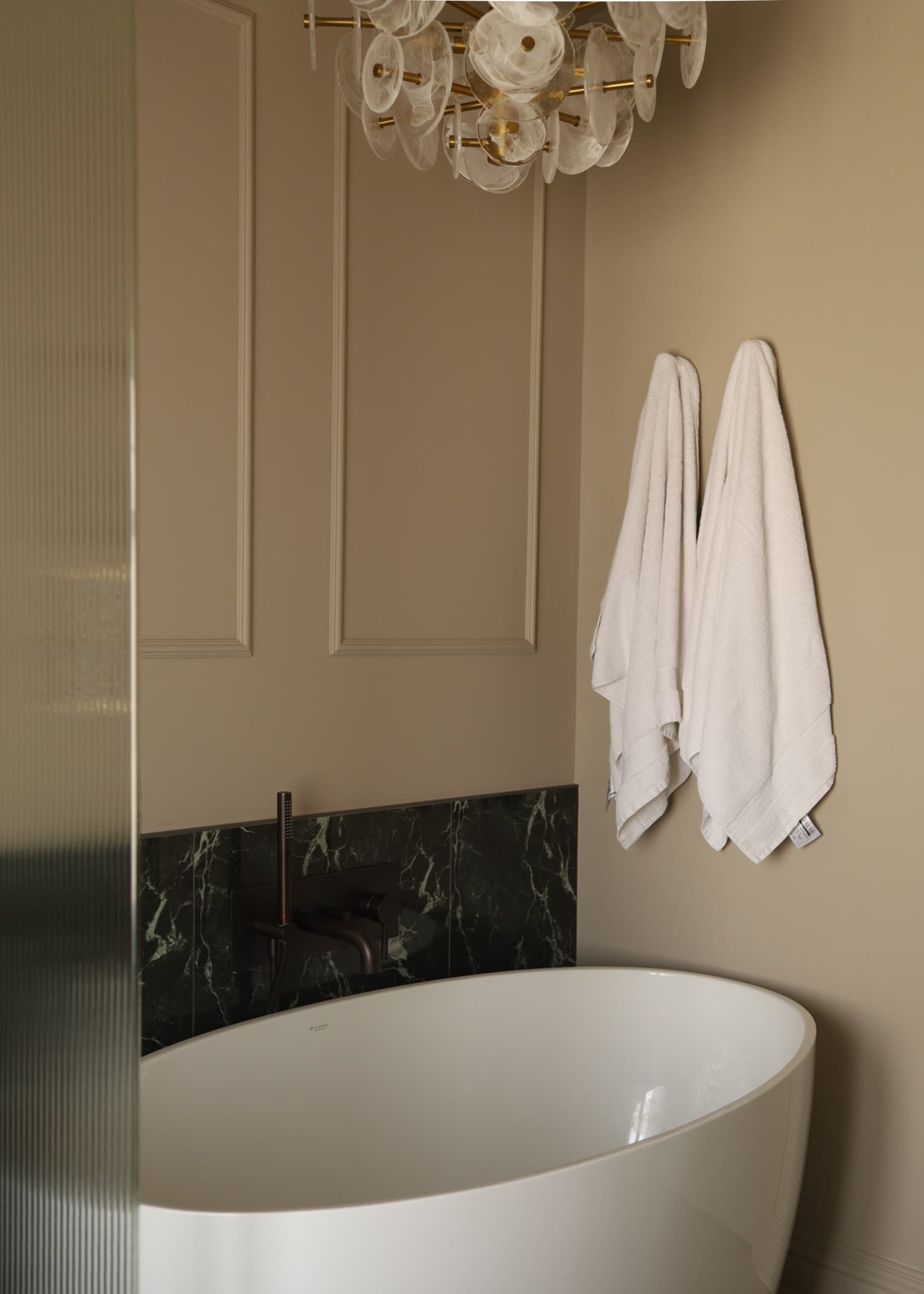 Baignoire blanche moderne avec dosseret en marbre noir, serviettes blanches et lustre décoratif élégant.