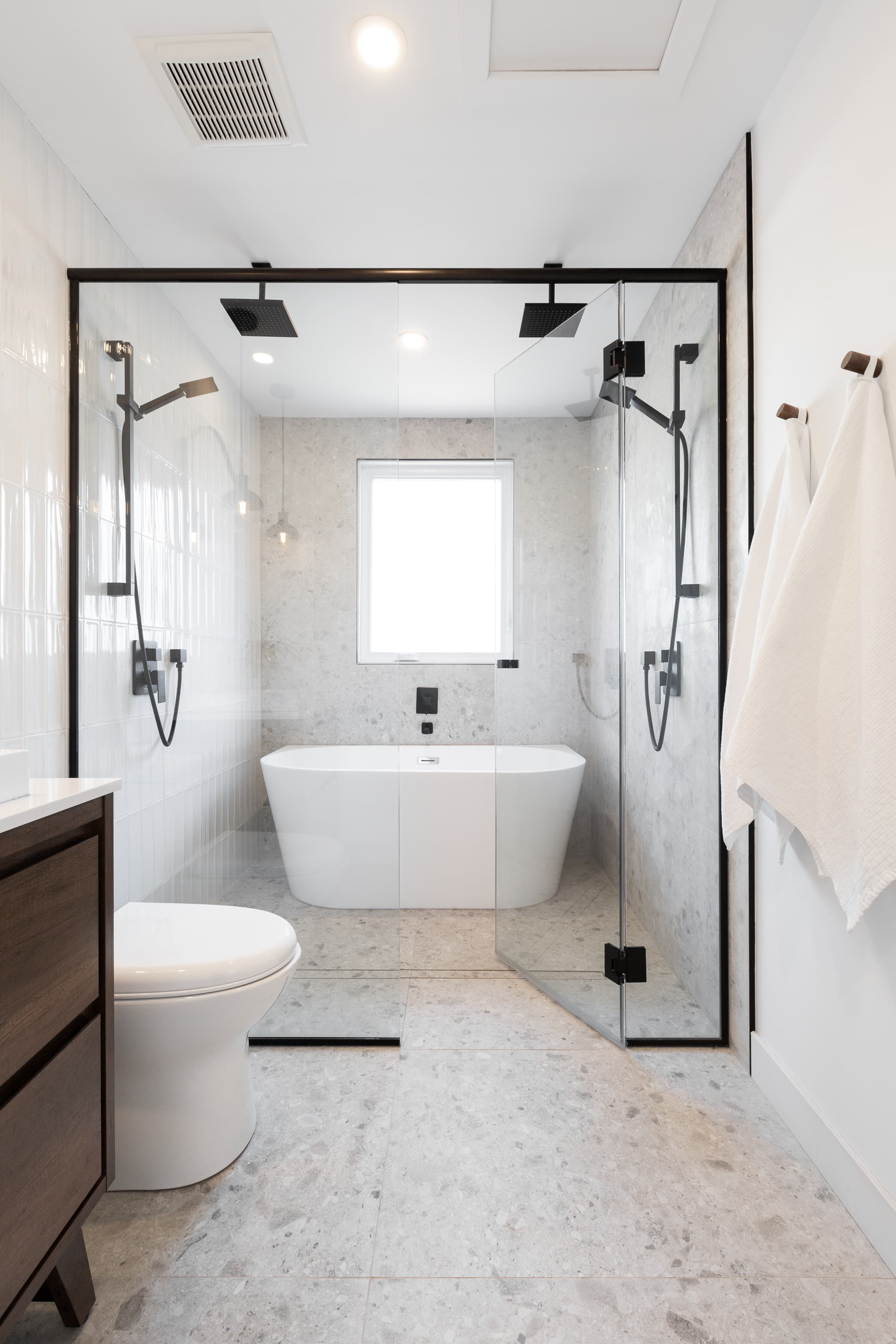 Salle de bain moderne avec douche vitrée, baignoire îlot, robinetterie noire et carrelage gris.